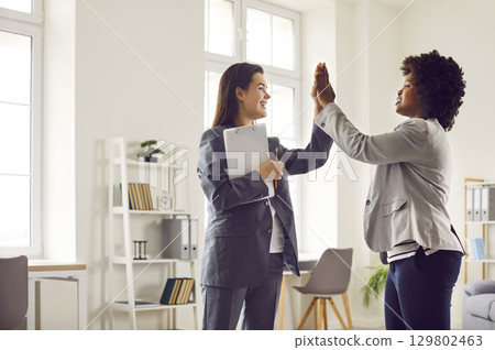 Two happy diverse business women making a deal and giving each other a high five 129802463