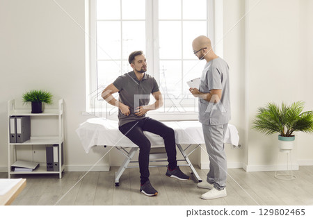 Man sitting in the doctor's office pointing to his stomach during medical examination in clinic Man sitting in the doctor's office pointing to his stomach during medical examination in clinic 129802465