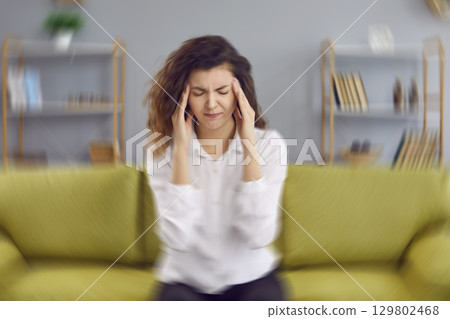 Woman sitting on the couch at home and feeling a dizzy, spinning sensation in her head Woman sitting on the couch at home and feeling a dizzy, spinning sensation in her head 129802468