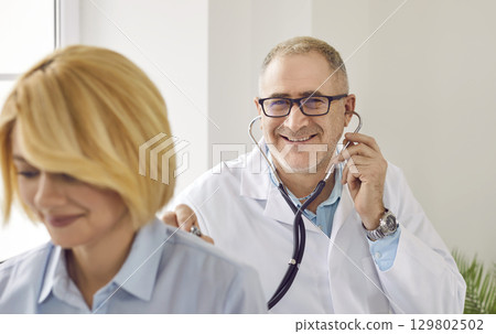Mature male doctor examining woman patient with stethoscope 129802502