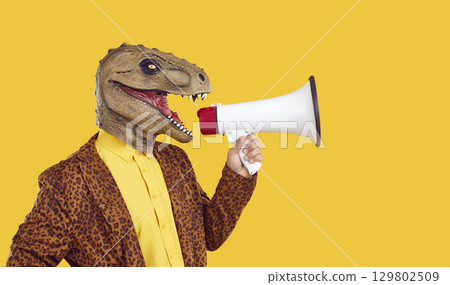 Man with funny dinosaur head speaks through megaphone on yellow color background 129802509