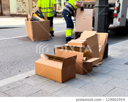 Workers dispose of cardboard boxes on city street sidewalk Workers dispose of cardboard boxes on city street sidewalk 129802954