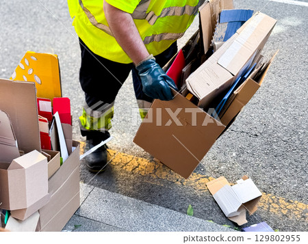 Male worker collecting cardboard boxes for recycling on street 129802955