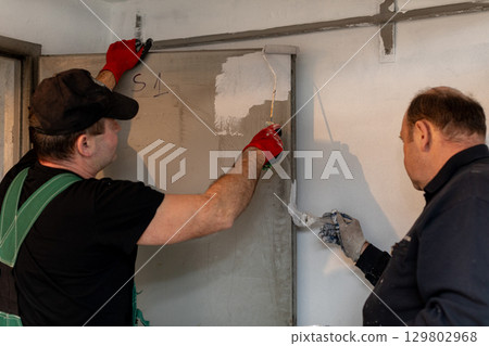 Workers are actively applying fresh paint meticulously on the wall for an improved finish Workers are actively applying fresh paint meticulously on the wall for an improved finish 129802968