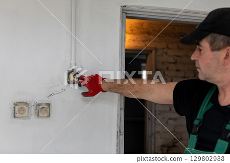 An Electrician Skillfully Installing a New Switch on the Wall in a Beautifully Renovated Room An Electrician Skillfully Installing a New Switch on the Wall in a Beautifully Renovated Room 129802988