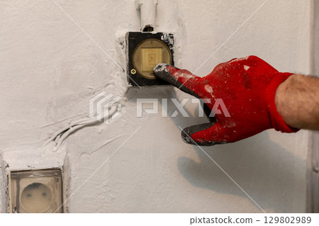 An electrician expertly repairing a switch mounted on the wall while wearing a protective glove An electrician expertly repairing a switch mounted on the wall while wearing a protective glove 129802989