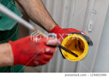 A Worker is Actively Preparing Bright Yellow Paint While Wearing Protective Gloves for Safety 129802990