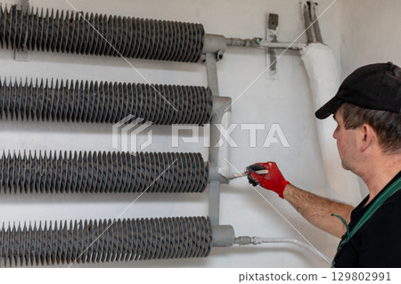 A skilled worker meticulously maintains painting equipment in an industrial setting for safety 129802991