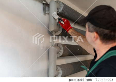 A skilled worker is carefully painting industrial pipes with precision in a modern workspace 129802993