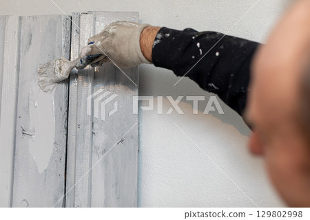 A skilled professional painter is meticulously applying a finish to a wall using a brush 129802998