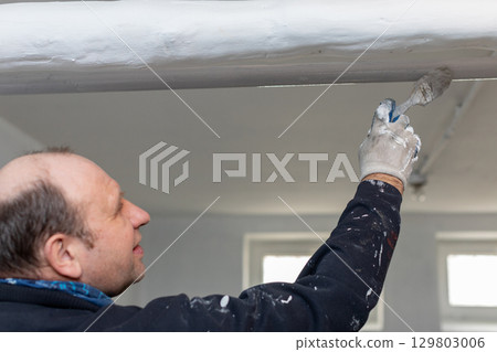 A skilled and professional painter is carefully applying the final finishing touches to the ceiling A skilled and professional painter is carefully applying the final finishing touches to the ceiling 129803006