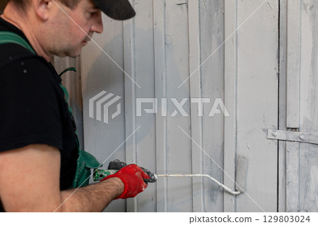 A man expertly painting a wall with a roller as part of a dedicated renovation project 129803024