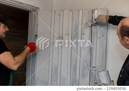 A group of men engaged in painting a wooden wall as part of their home renovation project A group of men engaged in painting a wooden wall as part of their home renovation project 129803036