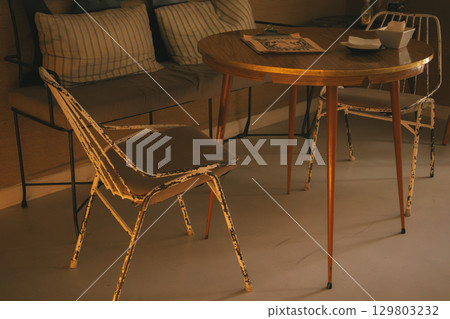 A charming vintage cafe setting with round table with shabby and rusty chairs. A cozy cafe corner with a vintage table and chairs, inviting you to relax and enjoy a moment of peace. Empty cafe scene. A charming vintage cafe setting with round table with shabby and rusty chairs. A cozy cafe corner with a vintage table and chairs, inviting you to relax and enjoy a moment of peace. Empty cafe scene. 129803232