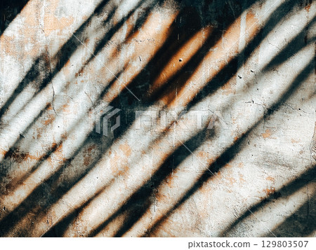Abstract textured wall with striking shadows from the sun, creating a visual contrast. The textured wall, sun-drenched, creates a play of light and shadow, highlighting the architectural details. Abstract textured wall with striking shadows from the sun, creating a visual contrast. The textured wall, sun-drenched, creates a play of light and shadow, highlighting the architectural details. 129803507