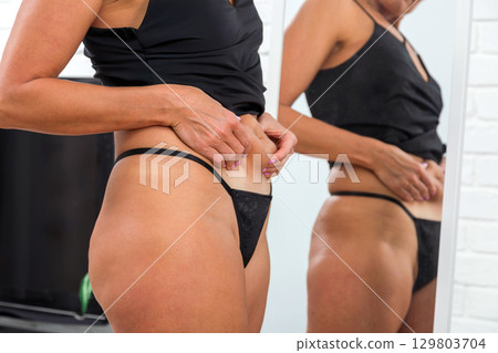 Woman in black underwear touching her belly in front of mirror at home 129803704
