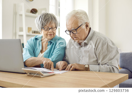 Senior couple sitting at the table and calculating finances or taxes at home. Senior couple sitting at the table and calculating finances or taxes at home. 129803736