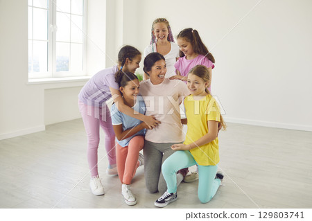 Happy girls dancers with theer teacher choreographer hugging together in dance studio. Happy girls dancers with theer teacher choreographer hugging together in dance studio. 129803741