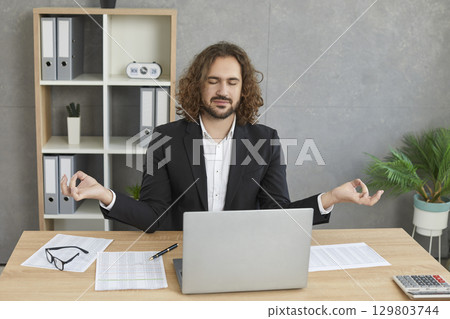 Young relaxed business man meditating and having a rest in the office on his workplace. Young relaxed business man meditating and having a rest in the office on his workplace. 129803744