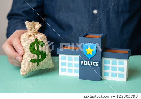 A man holds a dollar money bag near the police department building. A man holds a dollar money bag near the police department building. 129803798