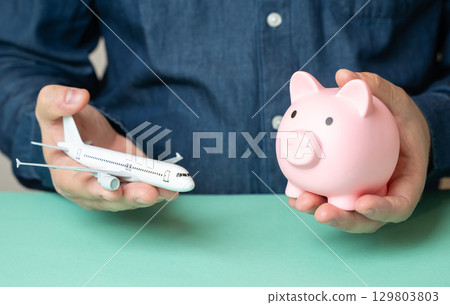 A man holds an airplane and a piggy bank. Travel savings. Budget flights. Cheap tickets. A man holds an airplane and a piggy bank. Travel savings. Budget flights. Cheap tickets. 129803803