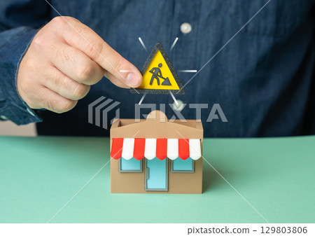 Man holding construction symbol above store. Construction and reconstruction of commercial premises. Man holding construction symbol above store. Construction and reconstruction of commercial premises. 129803806