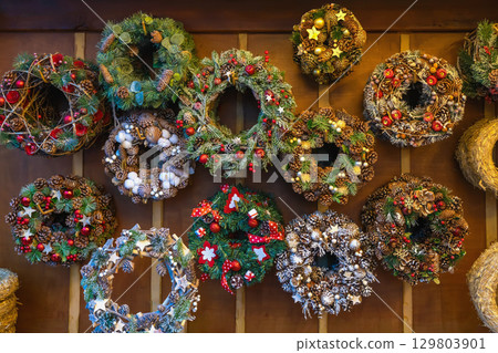 Christmas variety of decorated holiday wreaths. Handmade Christmas wreaths made of pine cones, berries, festive decorations on wooden wall. Concept of Christmas wreath, winter handmade holiday crafts 129803901