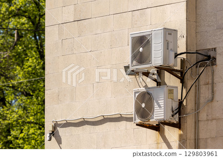 air conditioner on wall of an apartment building with view of green trees. air conditioner on wall of an apartment building with view of green trees. 129803961