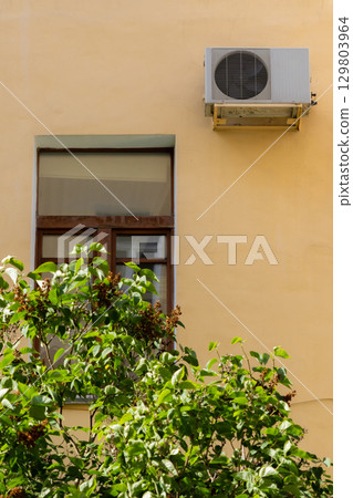 air conditioner on wall of an apartment building with view of green trees.  129803964