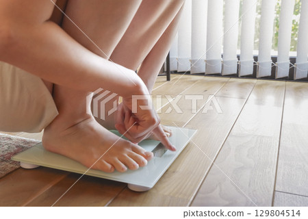 A woman measuring her weight on a scale 129804514