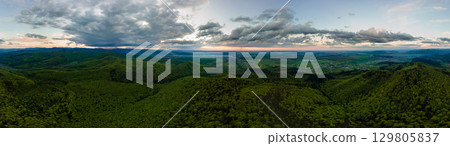 Aerial wide panoramic view of dark mountain hills covered with green mixed pine and lush forest in evening. Aerial wide panoramic view of dark mountain hills covered with green mixed pine and lush forest in evening. 129805837