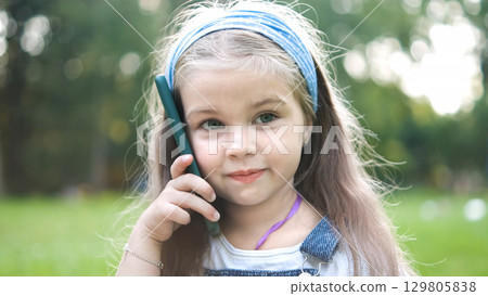 Happy little child girl having conversation talking on her sellphone in summer park. Happy little child girl having conversation talking on her sellphone in summer park. 129805838