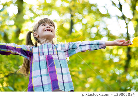 Portrait of happy pretty child girl having fun in autumn forest. Positive female kid enjoying warm day in fall park. 129805854