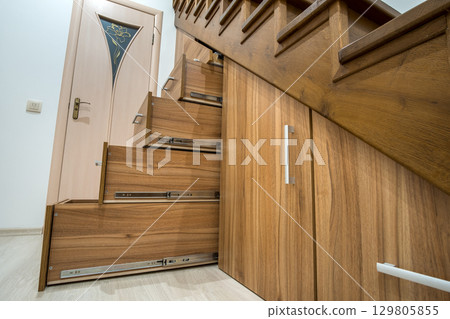Modern architecture interior with luxury hallway with glossy wooden stairs in multi-storey house. Custom built pullout cabinets on glides in slots under stairs. Use of space for storage. 129805855