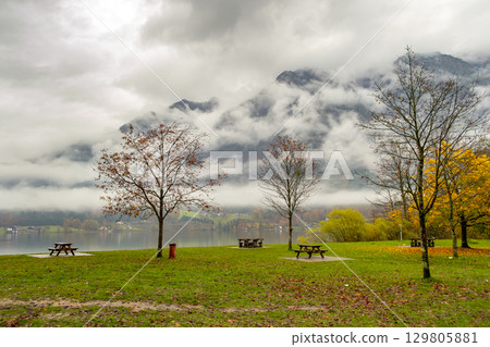 Moody autumn landscape with bare trees and benches on mountain lake shore. 129805881