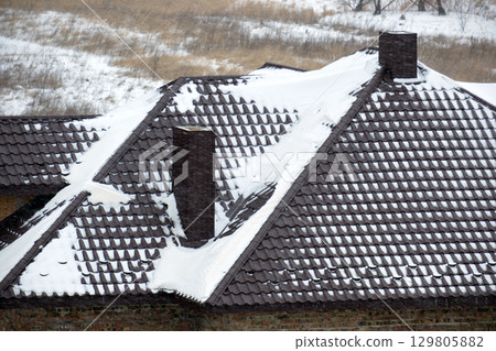Closeup of house roof top covered with snow in cold winter. Tiled covering of building in wintertime weather 129805882