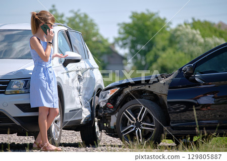 Stressed driver talking on sellphone on roadside near her smashed vehicle calling for emergency service help after car accident. Road safety and insurance concept Stressed driver talking on sellphone on roadside near her smashed vehicle calling for emergency service help after car accident. Road safety and insurance concept 129805887