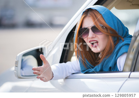Closeup portrait of pissed off displeased angry aggressive woman driving a car shouting at someone with hand fist up. Negative human expression consept. Closeup portrait of pissed off displeased angry aggressive woman driving a car shouting at someone with hand fist up. Negative human expression consept. 129805957