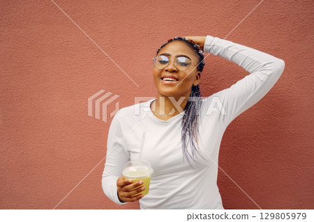 Young black woman with afro hairstyle smiling in a city. Mixed girl with cocktail. Young black woman with afro hairstyle smiling in a city. Mixed girl with cocktail. 129805979