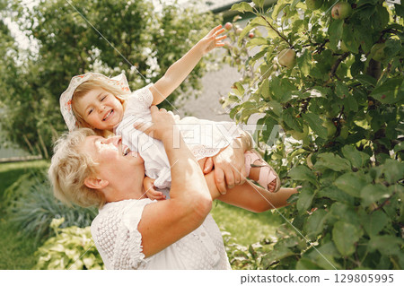 Grandmother and granddaughter together, hugging and joyfully laughing in a Flowering apricot garden in April. Family outdoors lifestyle. 129805995