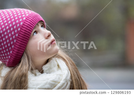 Pretty child girl in warm knitted winter clothes outdoors. 129806193