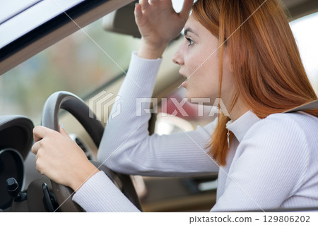 Sad tired yound woman driver sitting behind the car steering wheel in traffic jam. 129806202