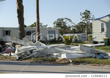 Heaps of debris rubbish on street side near severely damaged by hurricane houses in Florida mobile home residential area. Consequences of natural disaster 129806212