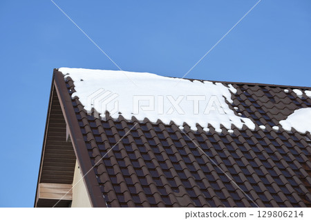 Closeup of house roof top covered with snow in cold winter. Tiled covering of building in wintertime weather 129806214