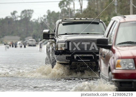Flooded Florida road with evacuating cars and surrounded with water houses in suburban residential area. Consequences of hurricane natural disaster 129806259
