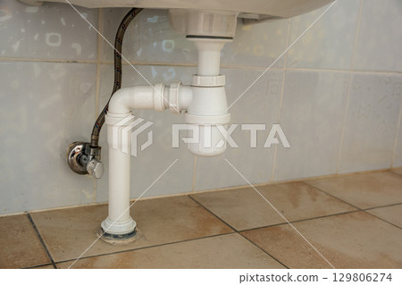 Close up of white plastic pipe drain under washing sink in bathroom. Close up of white plastic pipe drain under washing sink in bathroom. 129806274