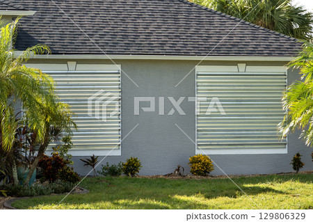 Storm resistant steel shutters cover windows of Florida house as precaution before hurricane. Home prepared for extreme weather Storm resistant steel shutters cover windows of Florida house as precaution before hurricane. Home prepared for extreme weather 129806329