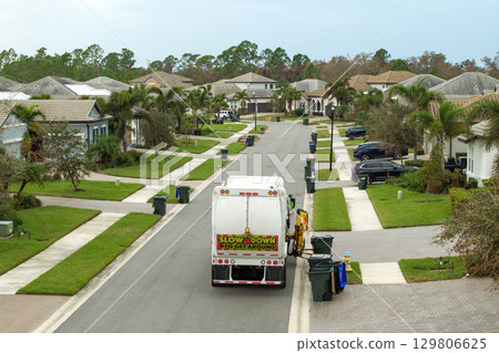 Garbage truck picking up trash bins on suburban street side 129806625