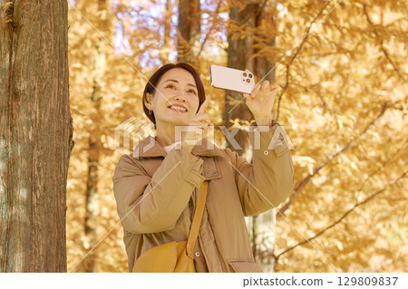 Middle-aged woman taking video of autumn leaves with her smartphone 129809837