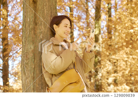Middle-aged woman using a smartphone among autumn leaves Middle-aged woman using a smartphone among autumn leaves 129809839